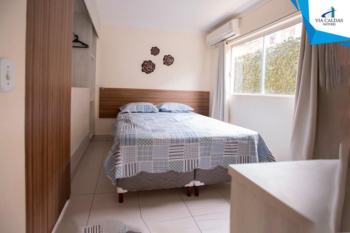 A bedroom with a bed, a window with curtains, a radiator, and a wall-mounted air conditioner.