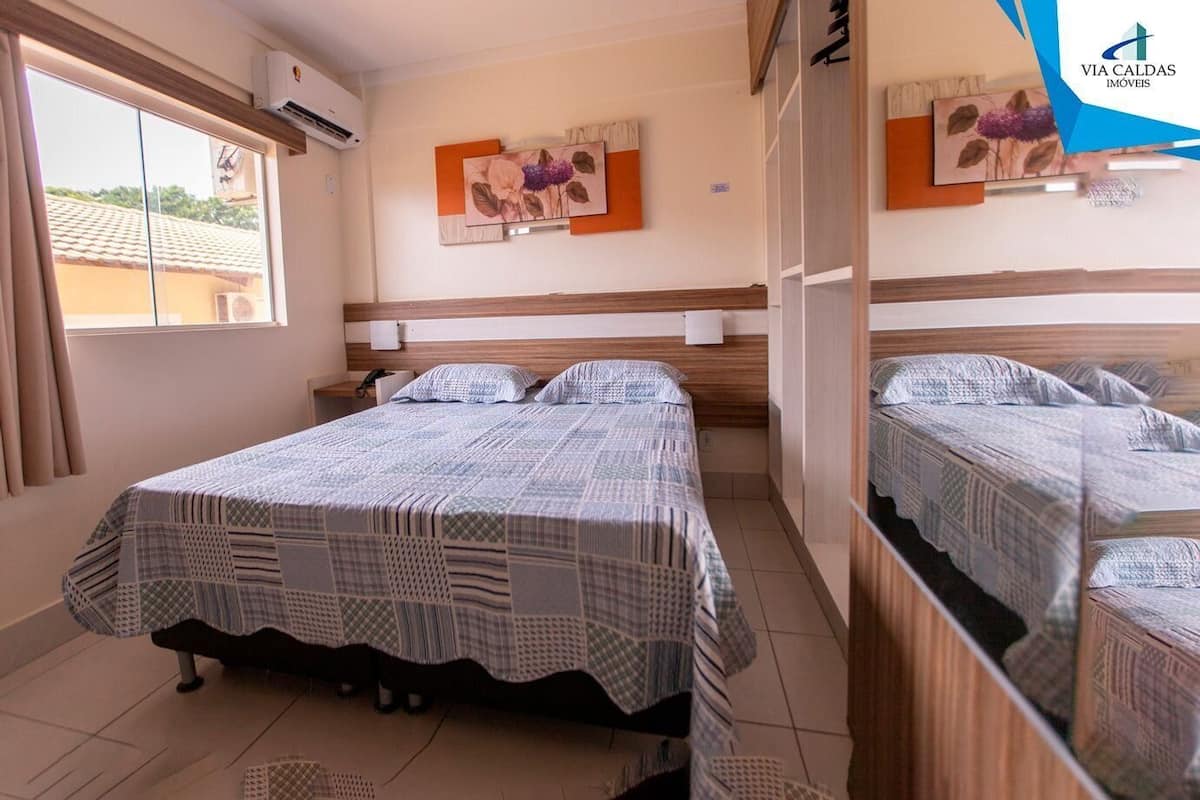 A bedroom with a bed, a nightstand, a mirror, and a window.