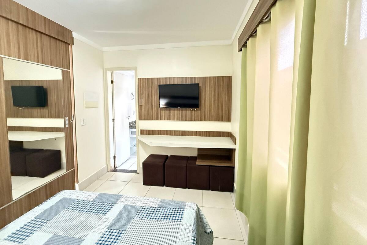 A bedroom with a bed, a TV mounted on the wall, a wardrobe, and a door leading to another room.
