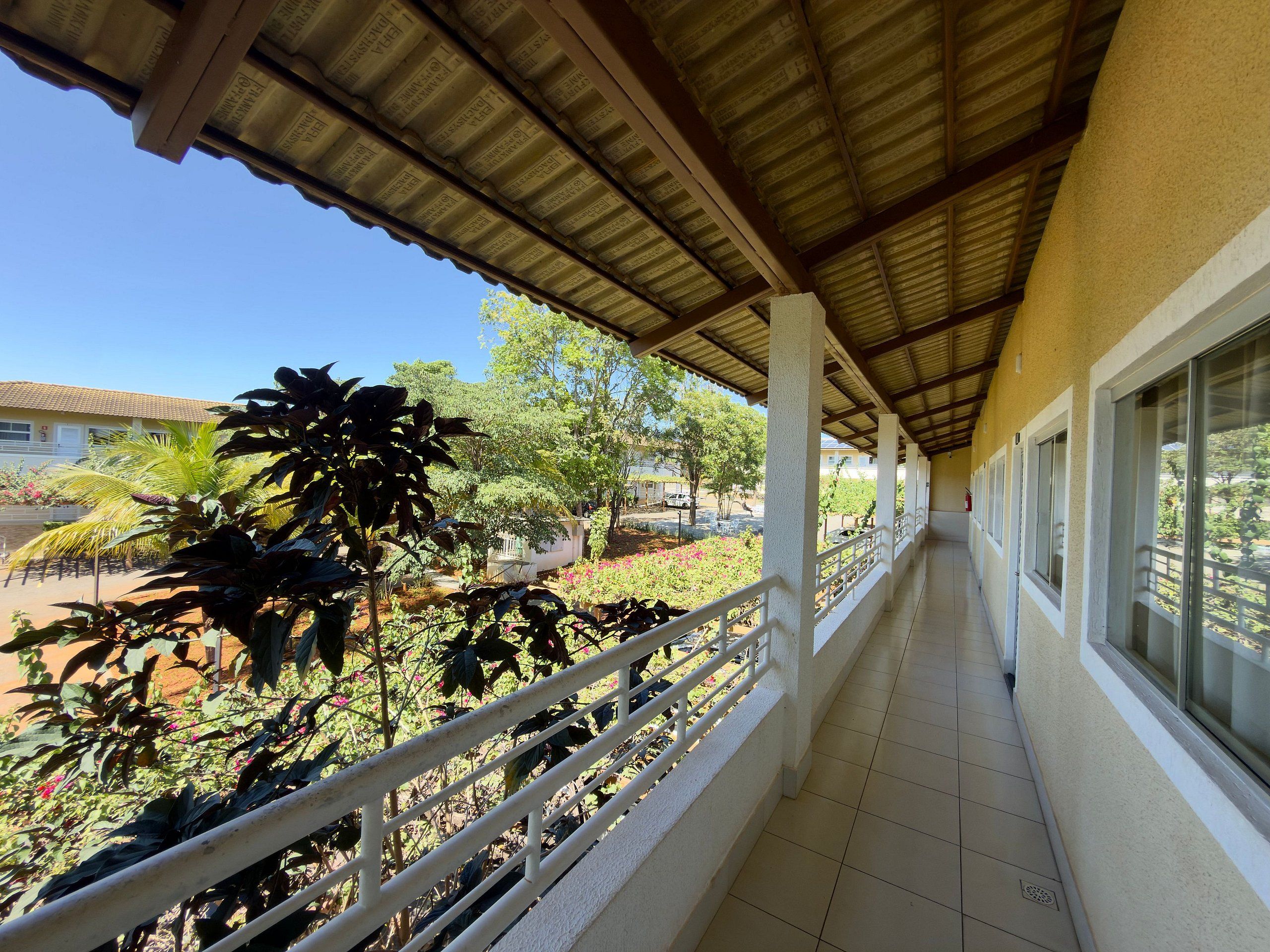 A covered corridor with a tiled floor, white railings, and large windows.