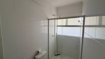 A bathroom with white tiled walls, a glass shower enclosure, a toilet, and a mop leaning against the wall.