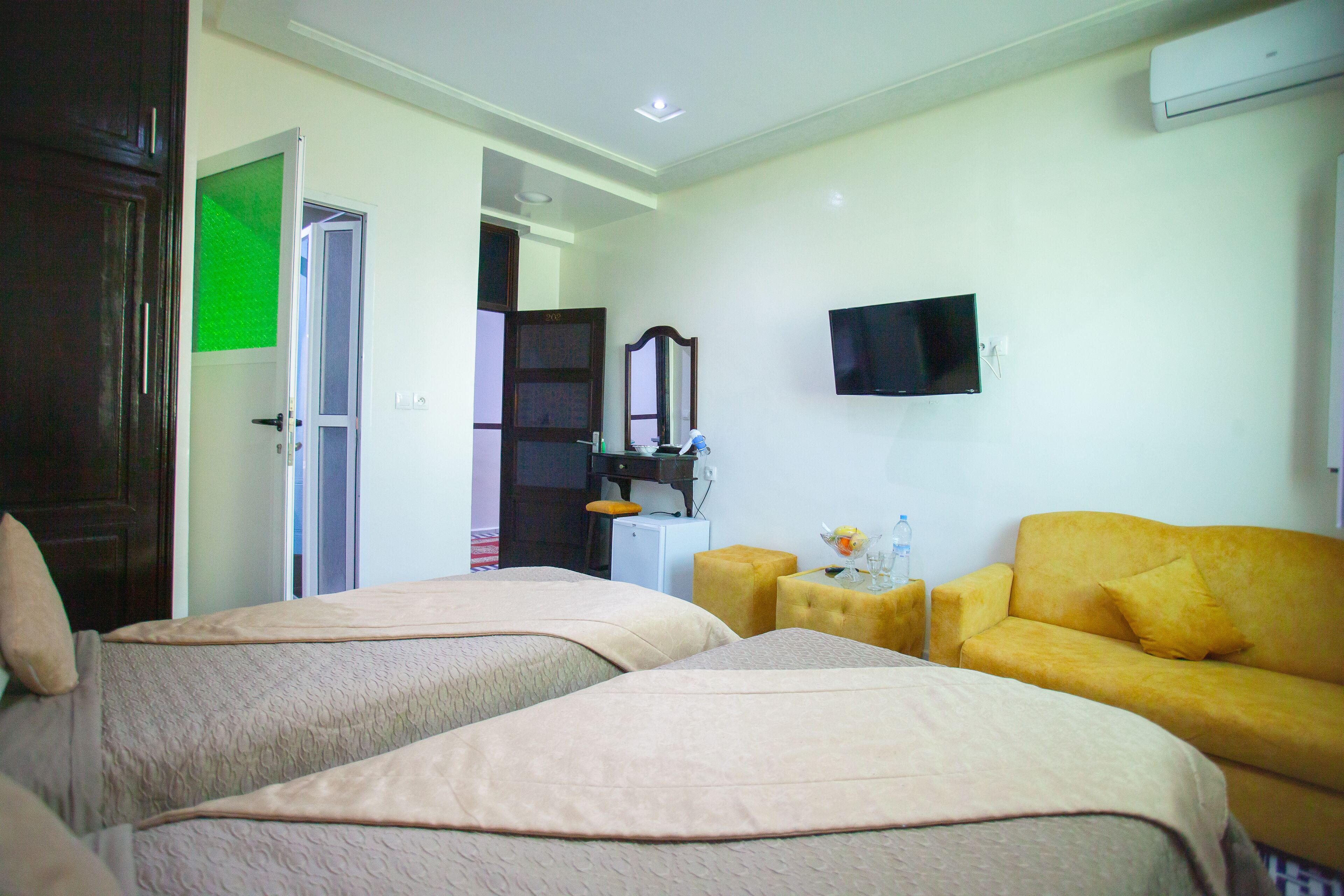 A hotel room with two beds, a sofa, a TV, and a mirror.