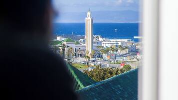A view from a window overlooking a cityscape with a prominent tower, a body of water, and a clear sky.