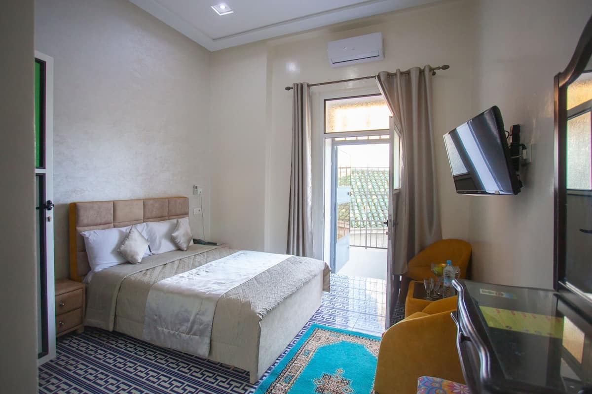 Habitación de hotel con cama, escritorio con silla, televisión y ventana con cortinas.