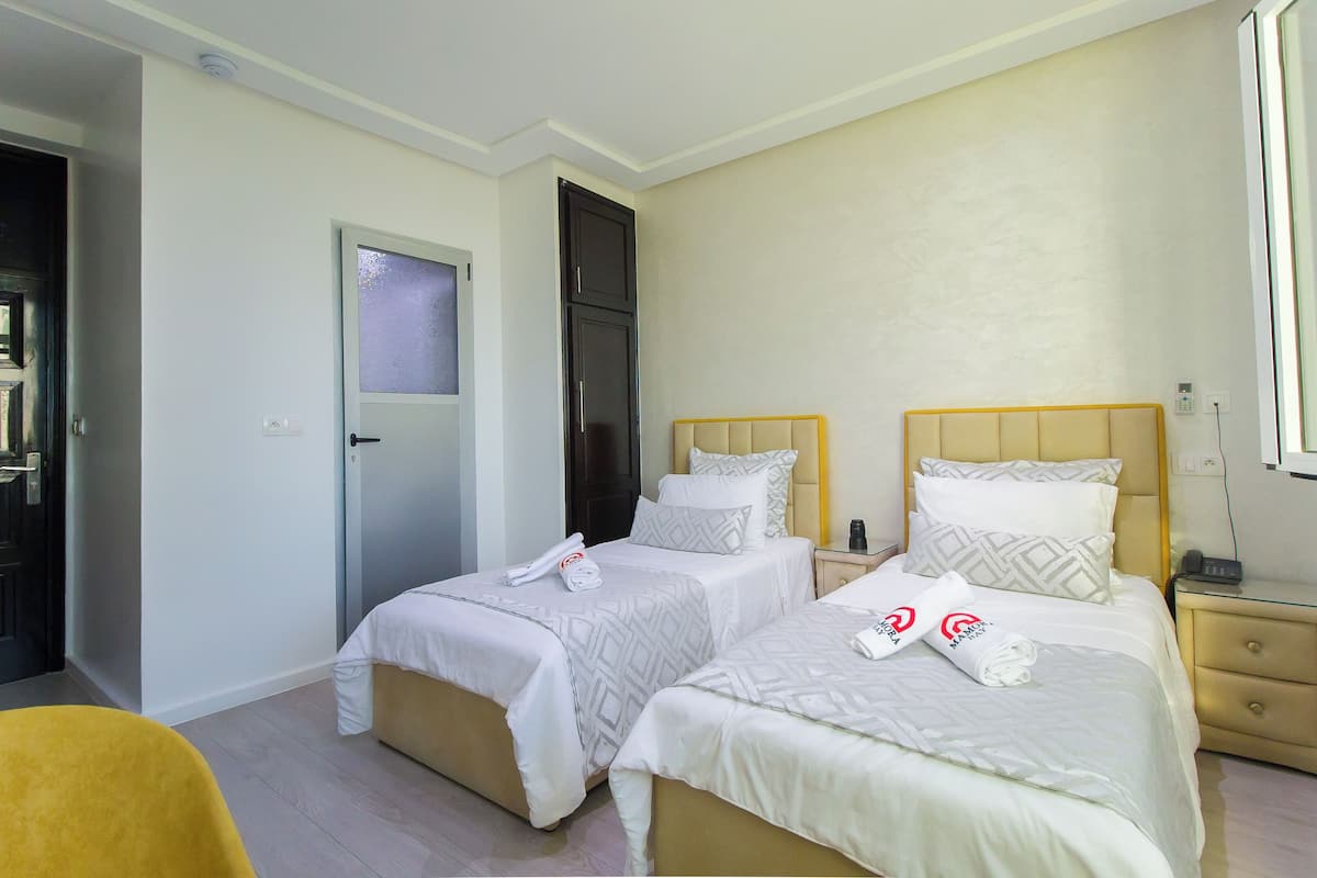 Habitación de hotel con dos camas individuales, una mesita de noche pequeña con teléfono y una puerta con vidrio esmerilado.