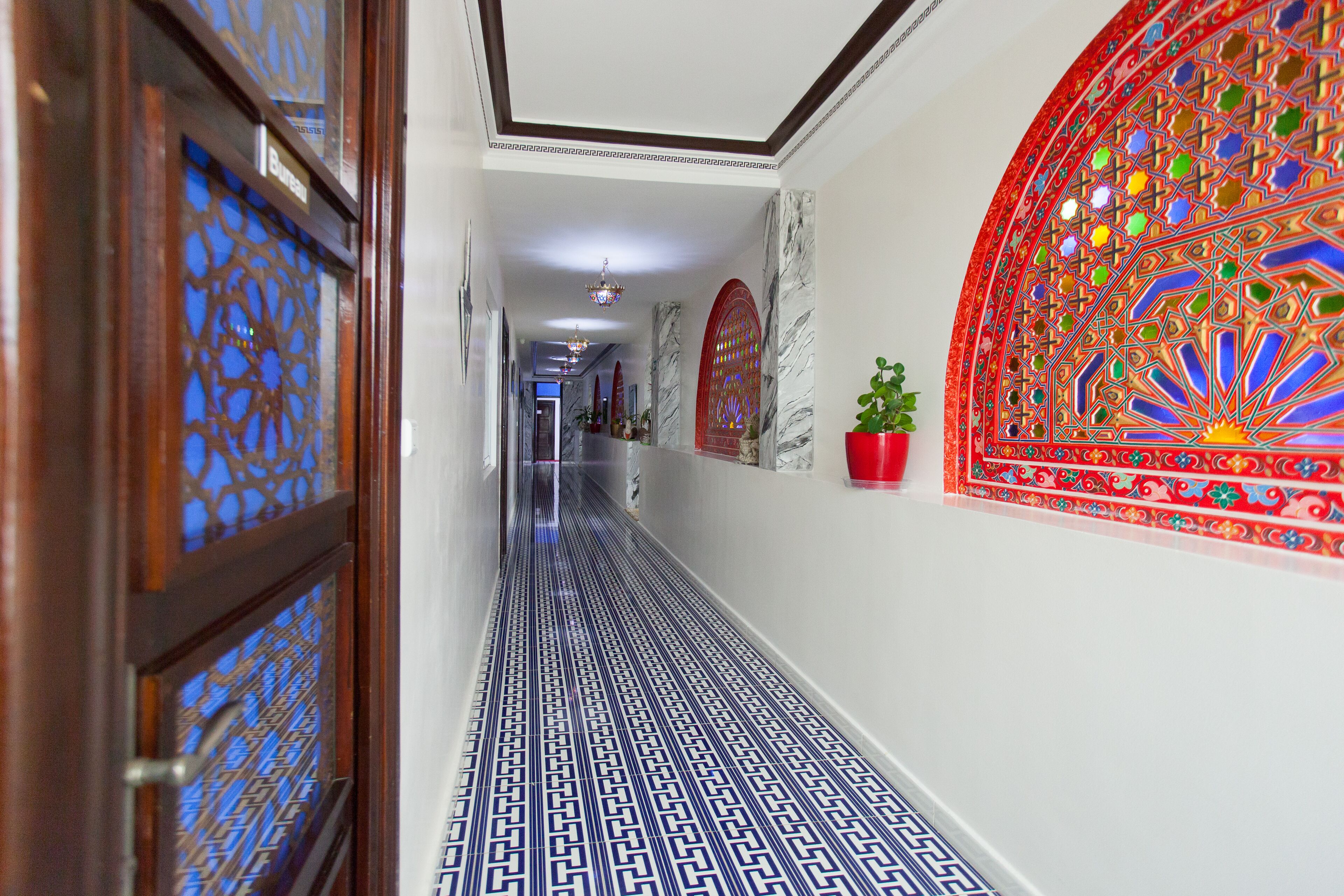A hallway with patterned flooring, decorative wall panels, and a potted plant.