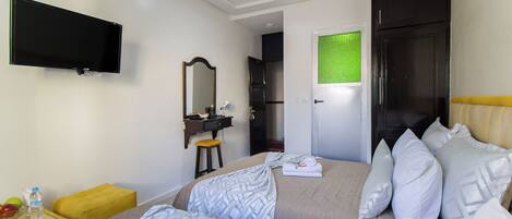 A hotel room with a bed, a TV mounted on the wall, a desk with a chair, and a mirror.