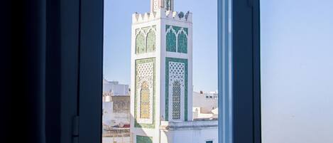 A window with a view of a building featuring a tower with intricate patterns and a spire.