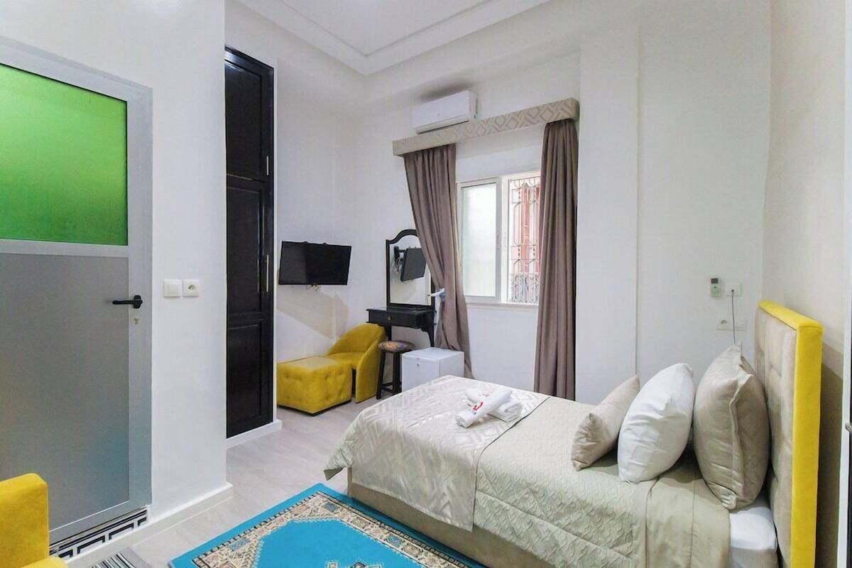 Habitación de hotel con cama, escritorio, silla, televisión y ventana con cortinas.