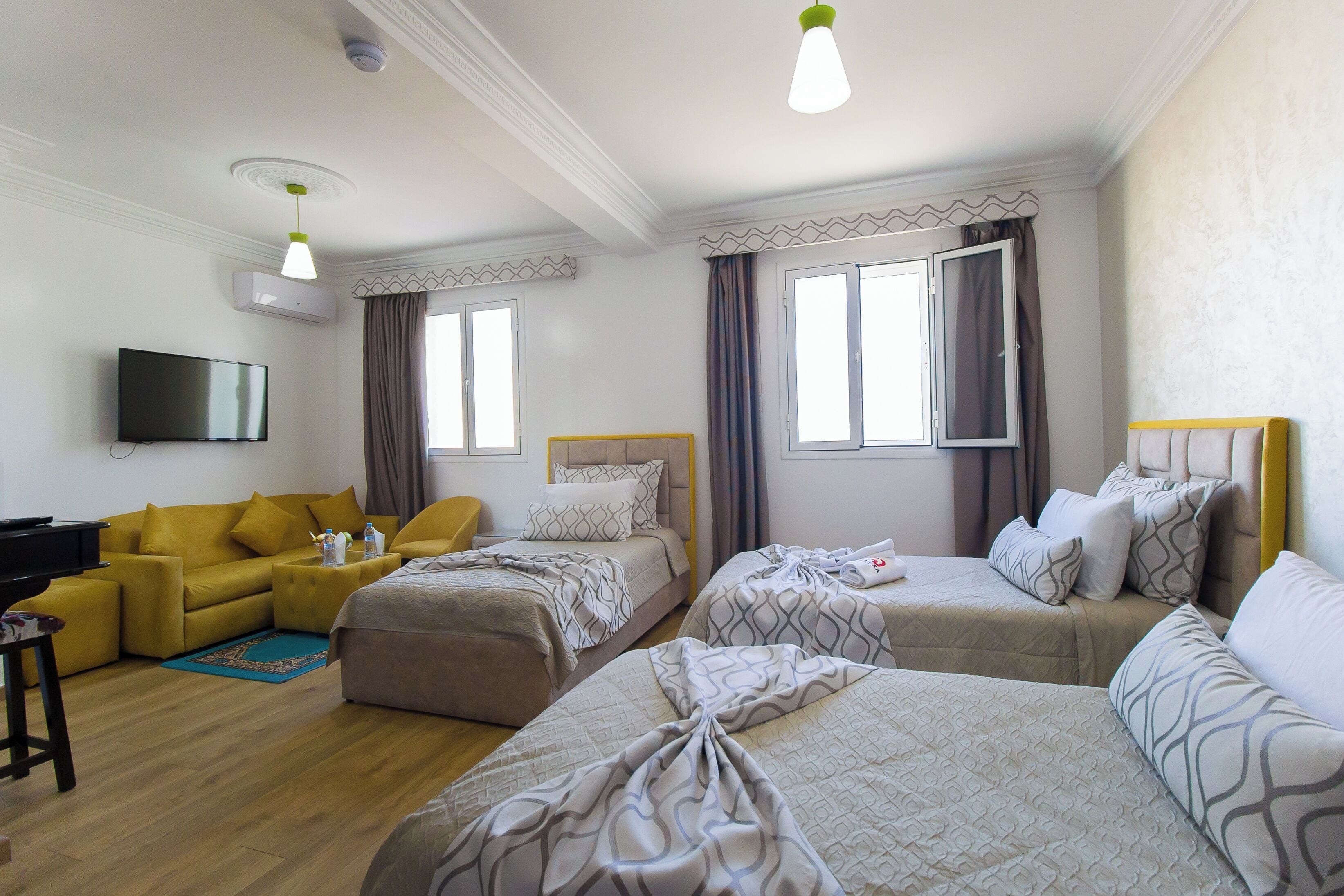 Una habitación de hotel con un sofá amarillo, dos camas individuales, una televisión y un televisor de pantalla plana montado en la pared.