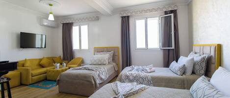 Een hotelkamer met een gele bank, twee eenpersoonsbedden, een televisie en een flatscreen aan de muur.