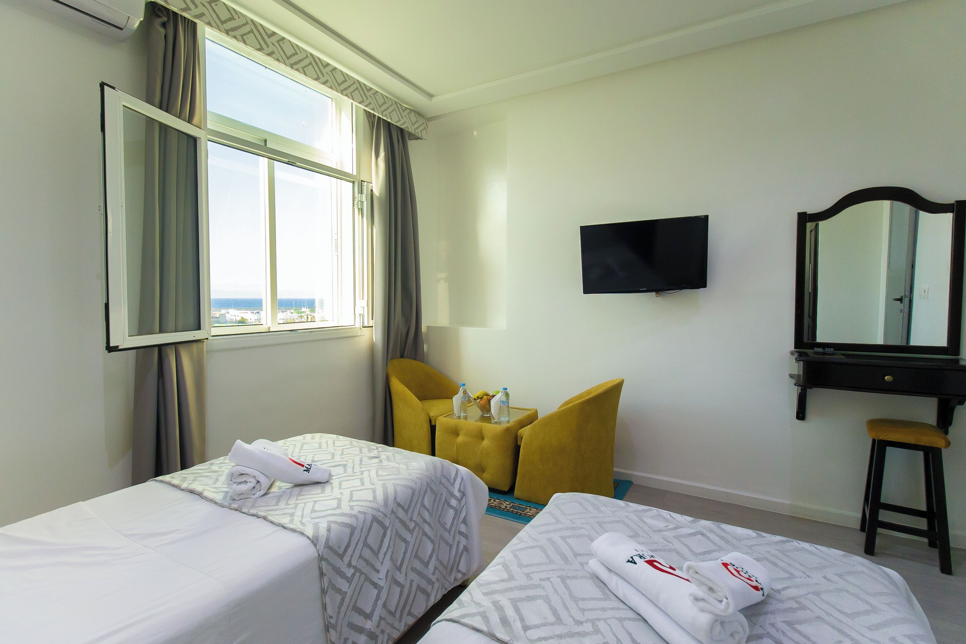 Una habitación de hotel con dos camas, televisión, espejo y ventana con cortinas.