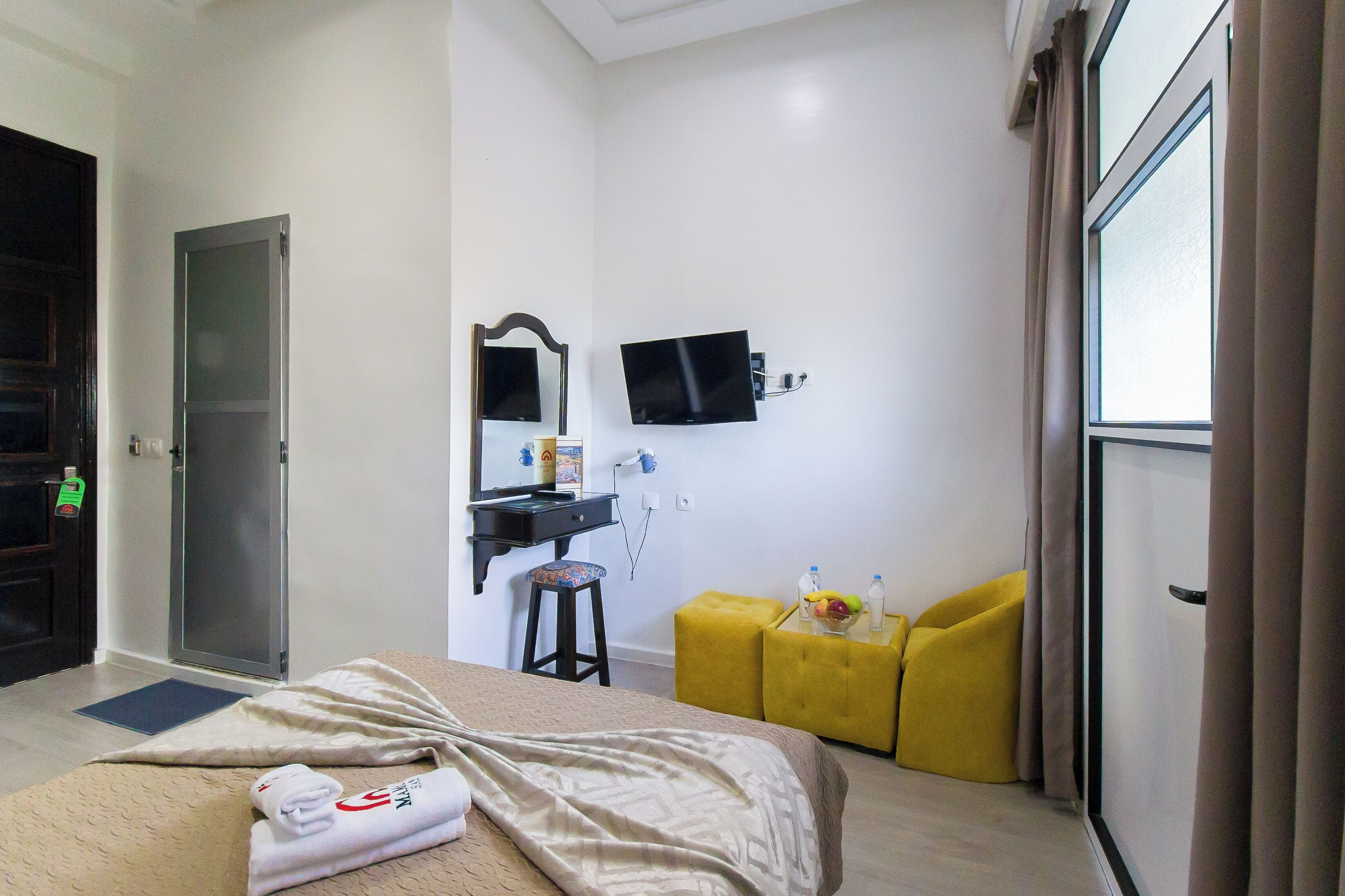 A hotel room with a bed, a desk with a mirror, a television, and a window with curtains.
