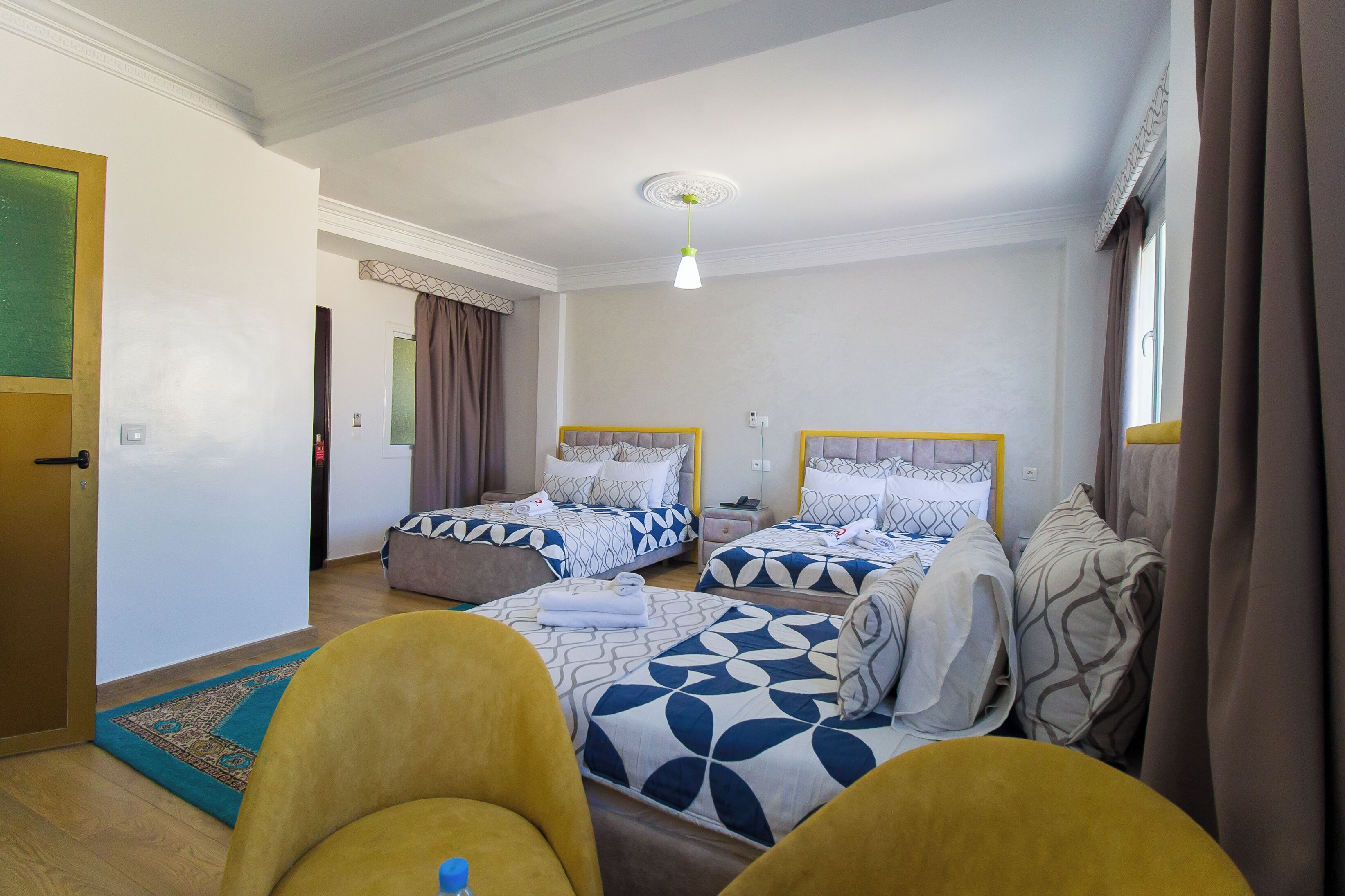 A hotel room with two beds, a sofa, a small table, and a window with curtains.