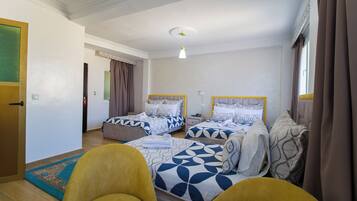 Habitación de hotel con dos camas, un sofá, una mesita y una ventana con cortinas.