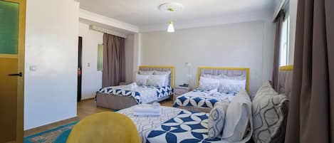 A hotel room with two beds, a sofa, a small table, and a window with curtains.