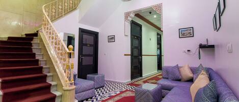 Uma escadaria com corrimão estampado, um sofá roxo e um tapete com padrão em um quarto com paredes brancas e teto decorado.