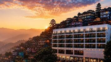 A multi-story hotel with balconies, set against a backdrop of a mountainous landscape during sunset.