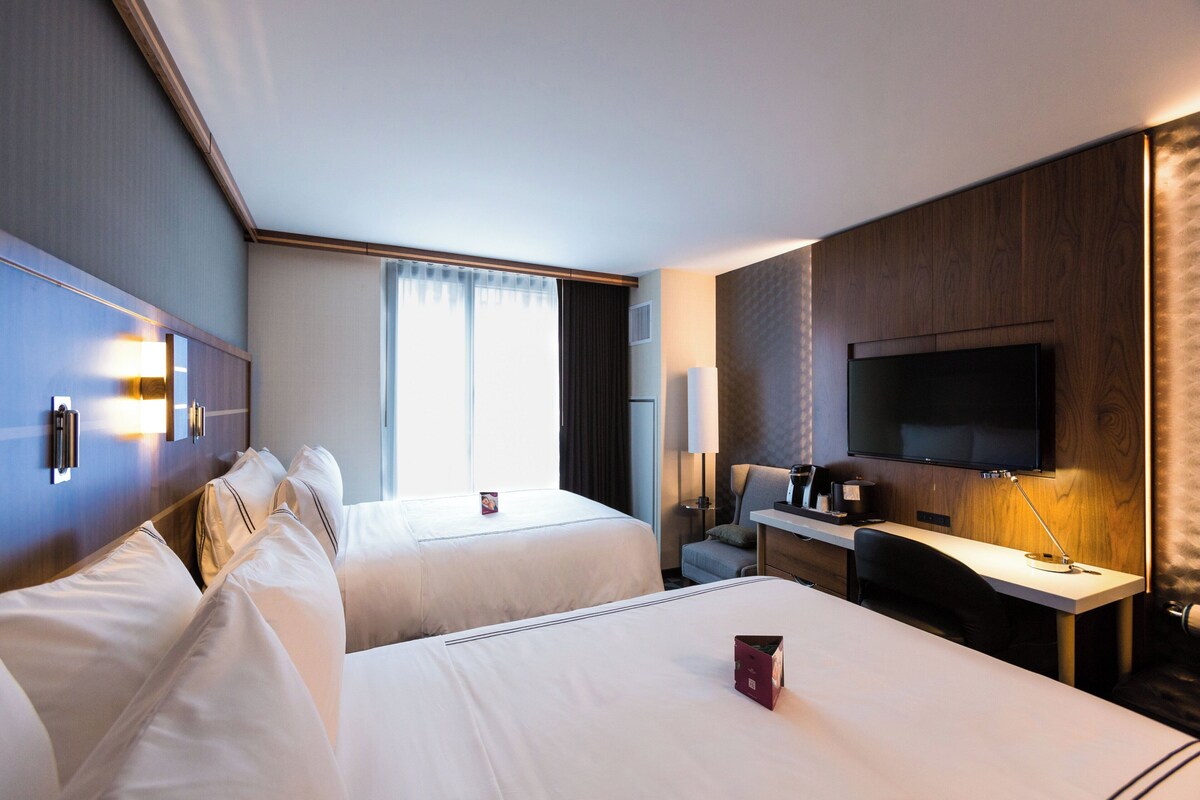 Habitación de hotel con dos camas, un escritorio, un televisor y una ventana con cortinas.