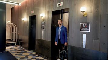 A man exiting an elevator in a hotel lobby with a sign indicating the first floor and a fire safety instruction.