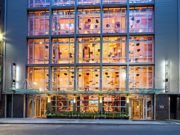 Un hotel de varios pisos con fachada de vidrio, ventanas amplias y una entrada moderna con marquesina de cristal.
