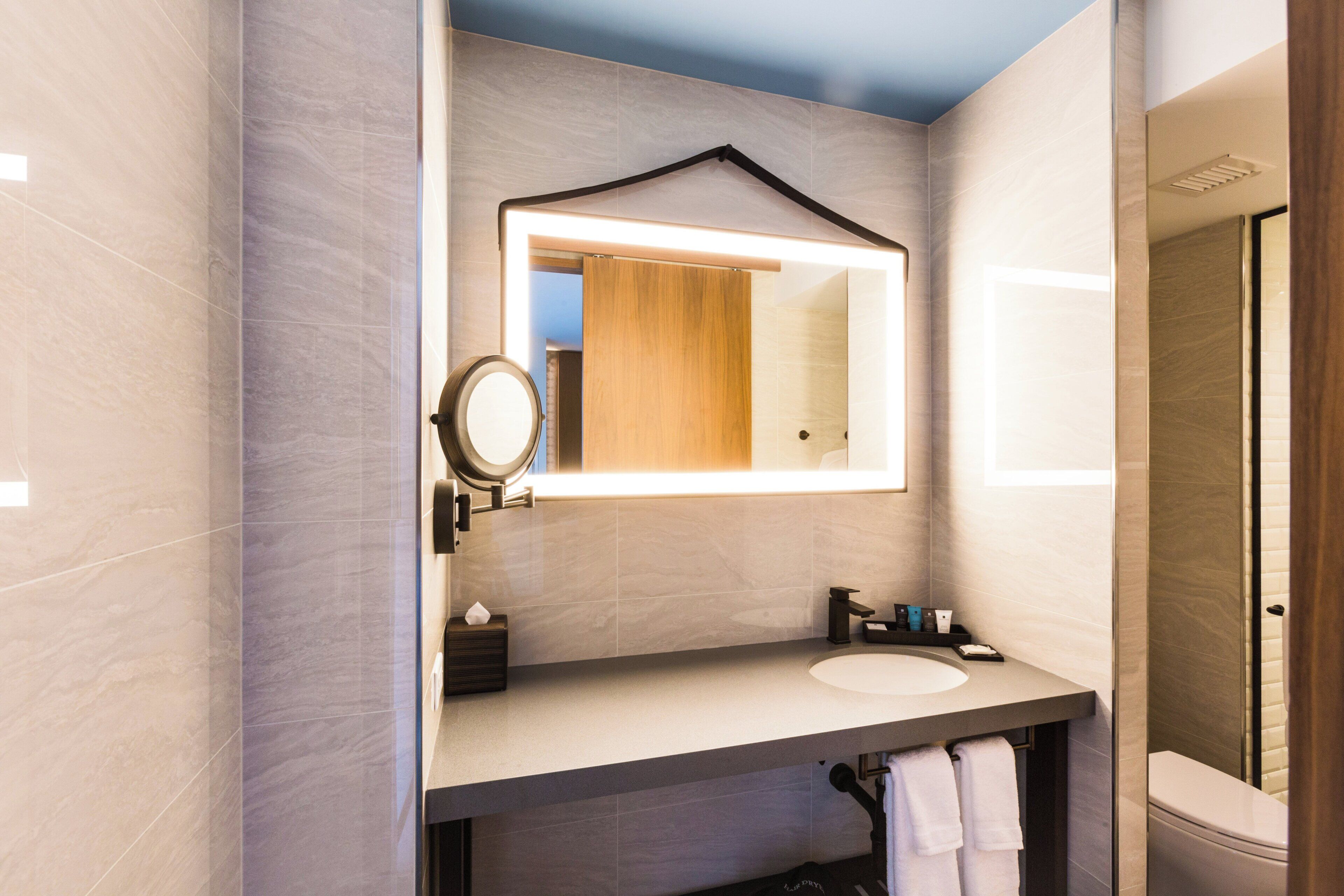 A modern bathroom with a large mirror, a round mirror, a sink, and a toilet.