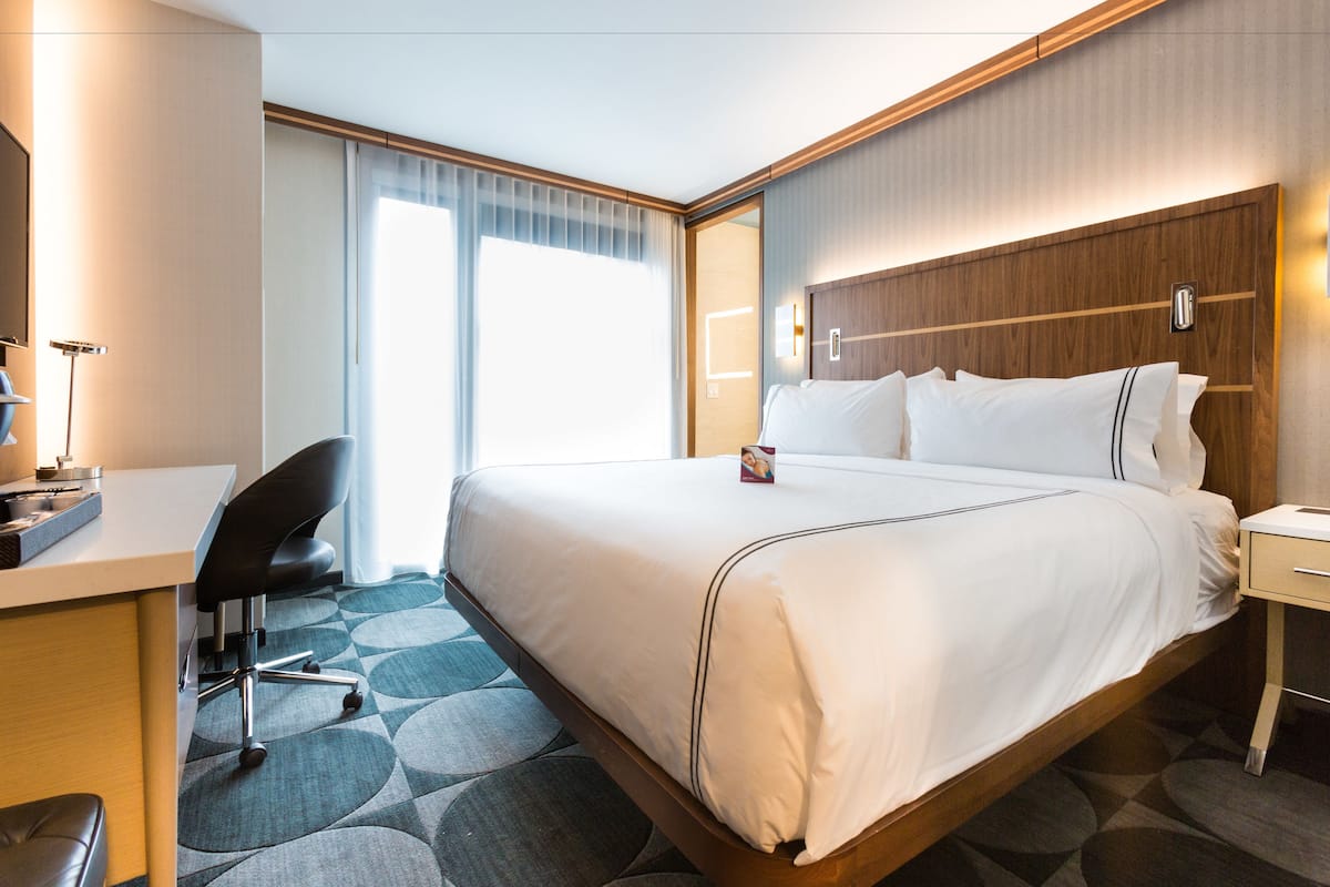 Ein Hotelzimmer mit einem großen Bett, einem Schreibtisch, einem Sessel und einem Nachttisch.