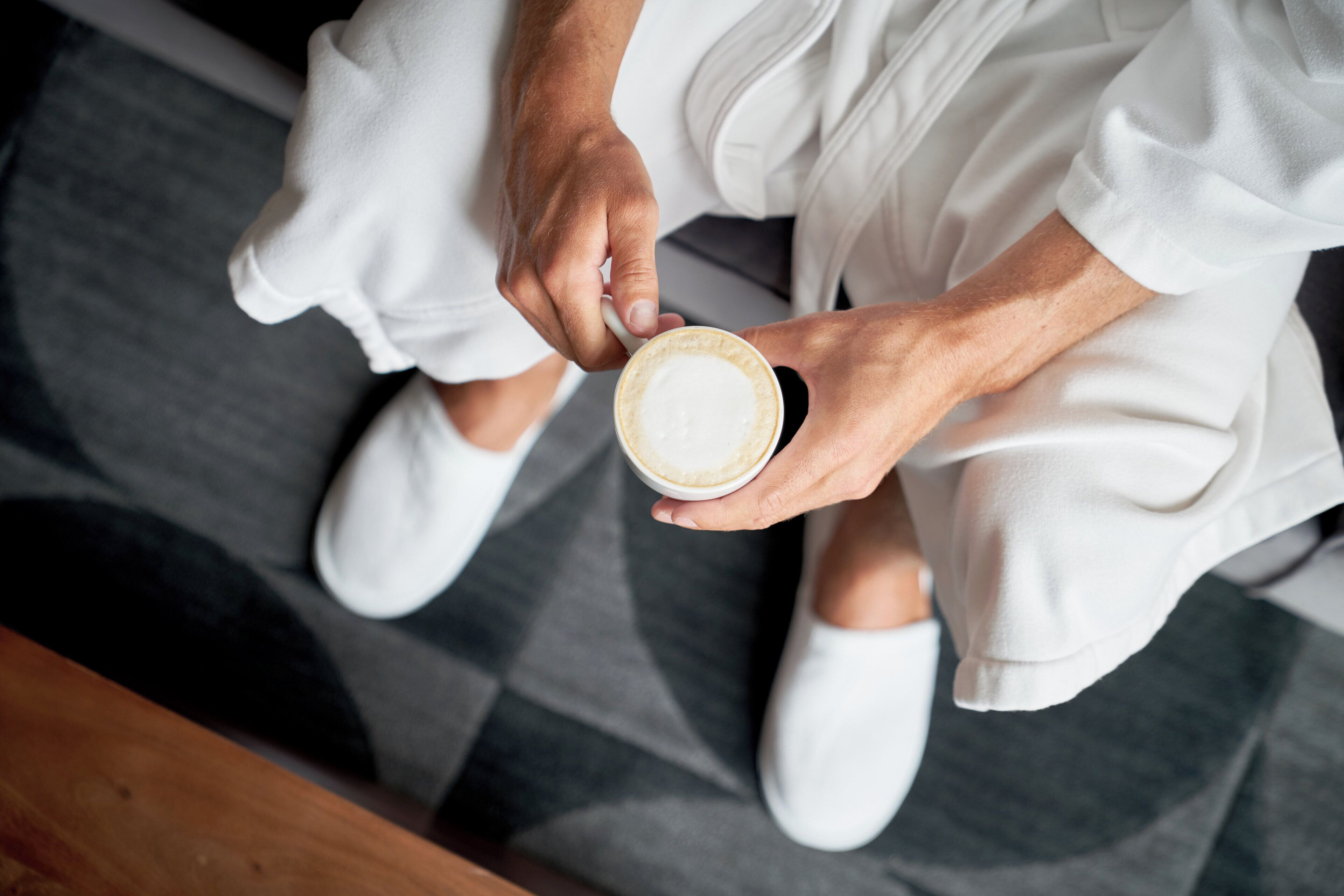 A person holding a cup of coffee, seated on a patterned floor.
