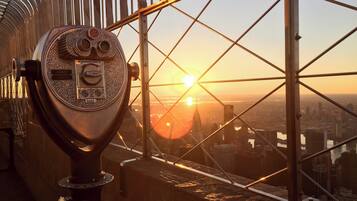 Un télescope ancien, agrémenté d’une plaque commémorative, est placé près d’une grande fenêtre donnant sur un paysage urbain au coucher du soleil.