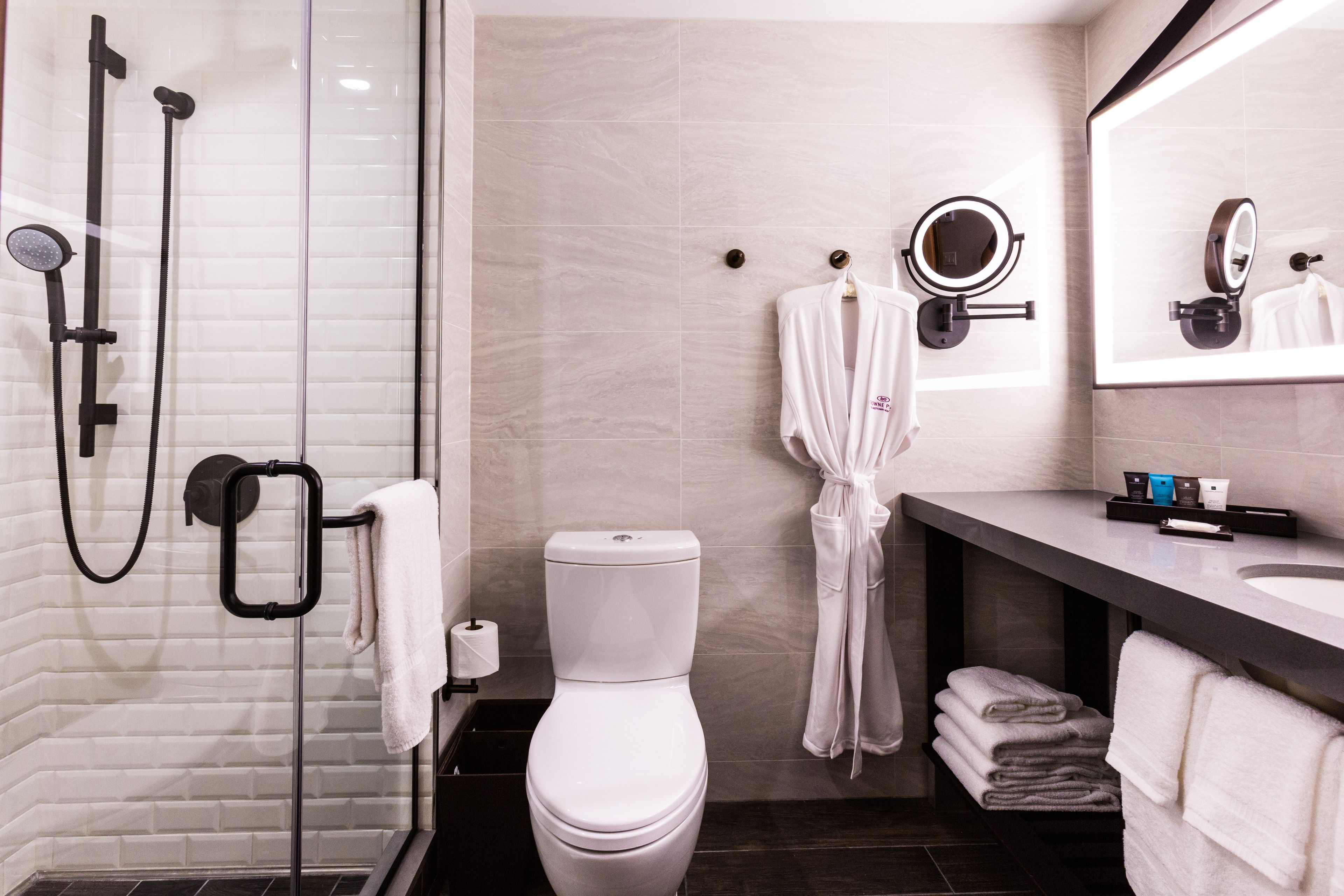 A modern bathroom with a glass-enclosed shower, a toilet, a vanity with a mirror, and neatly stacked towels.
