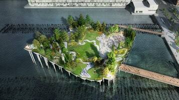 An aerial view of a waterfront property with a central island featuring a park, pathways, and a bridge connecting to the main land.