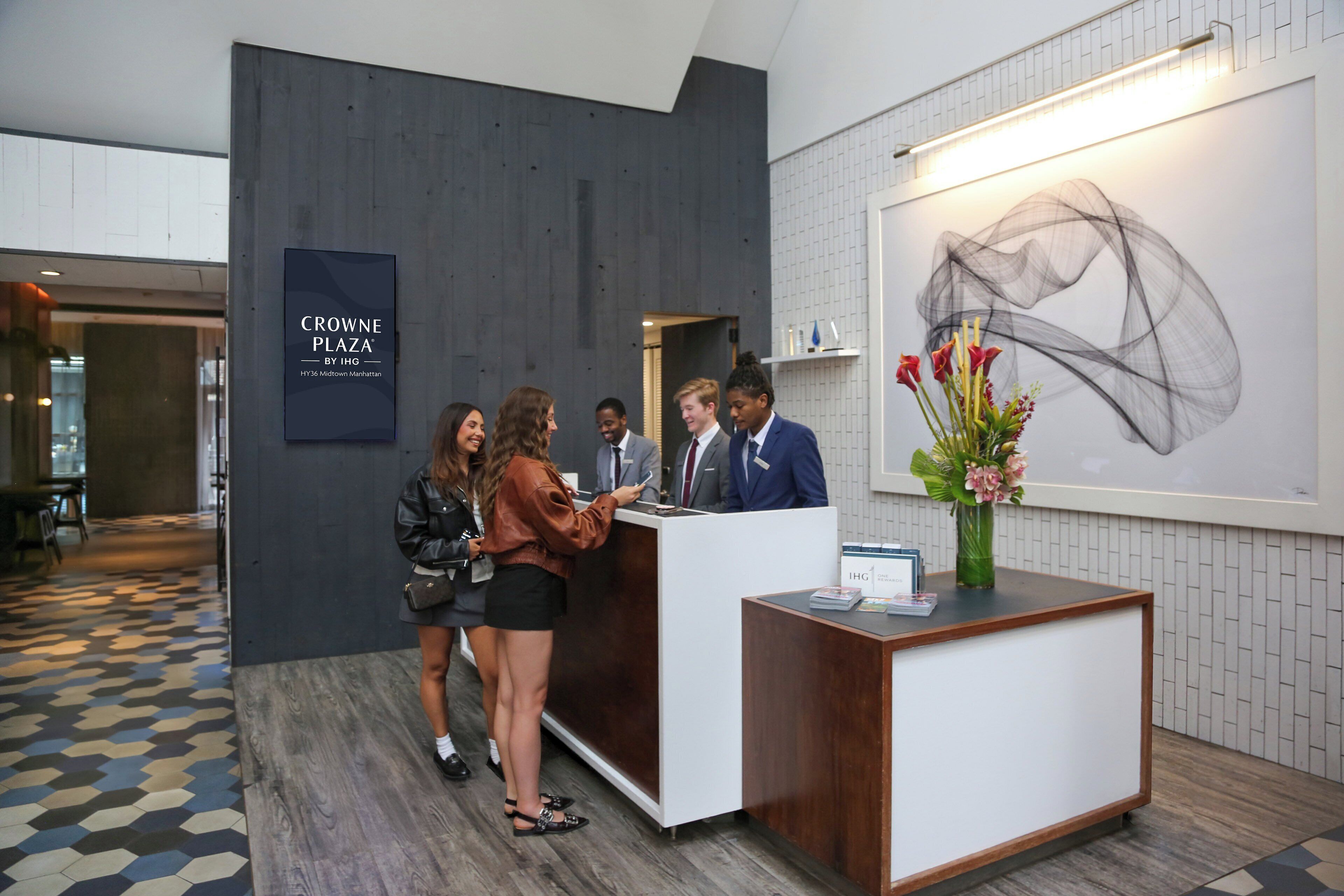A reception area with a modern design, including a reception desk, a wall-mounted artwork, and a sign indicating the location as Crowne Plaza by IHG.