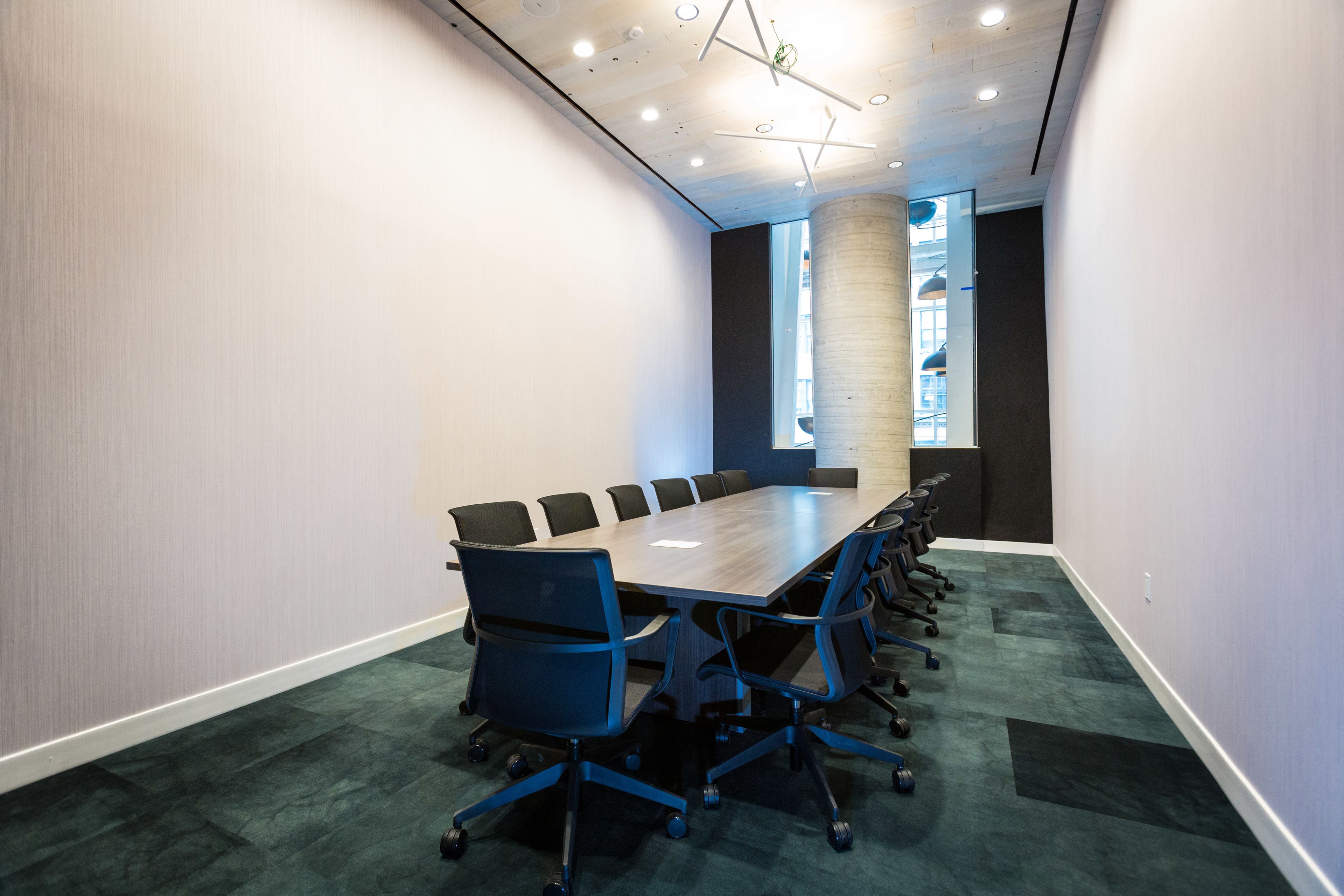 A conference room with a long table, multiple chairs, and a carpeted floor.