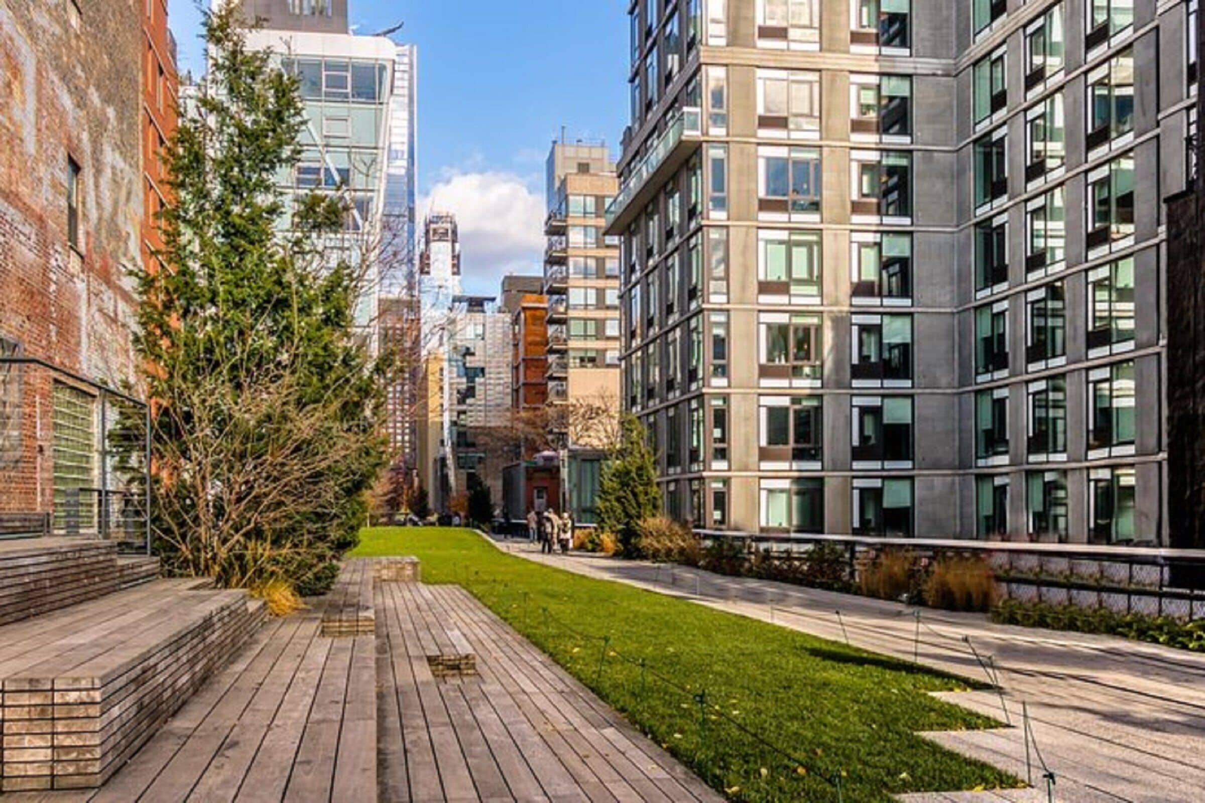 Una calle urbana moderna con una acera pavimentada, edificios con grandes ventanales y un pequeño espacio con césped.