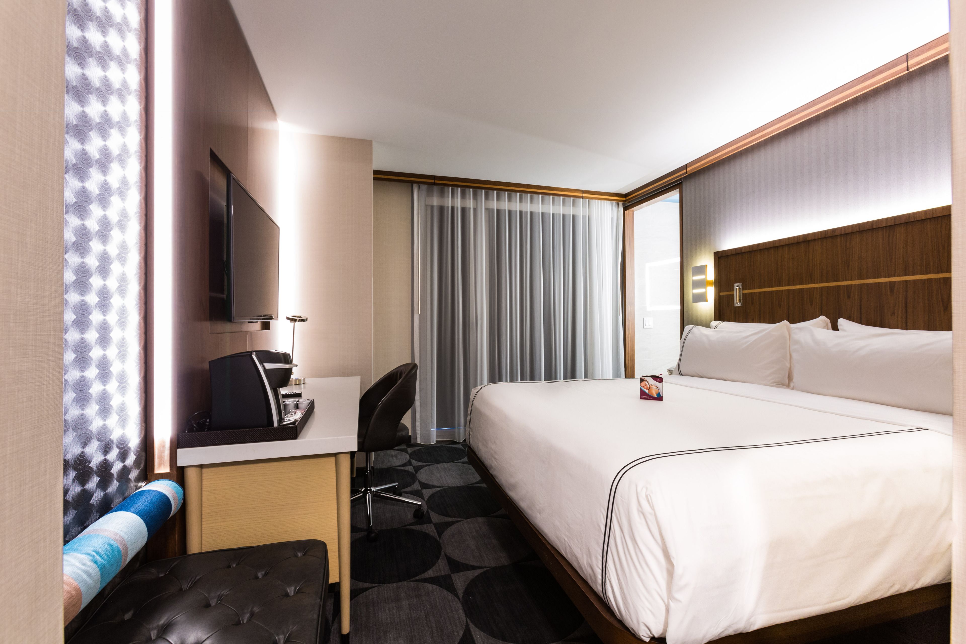 A hotel room with a bed, a desk, a chair, a television, and a window with curtains.