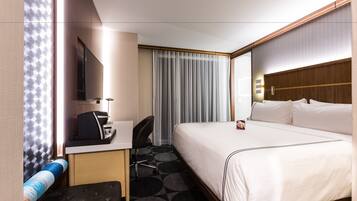 A hotel room with a bed, a desk, a chair, a television, and a window with curtains.
