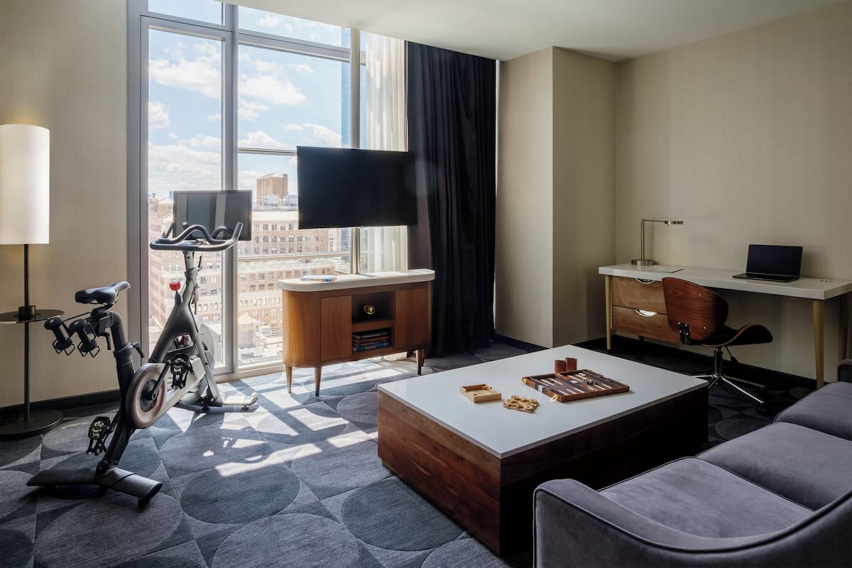 Ein modernes Hotelzimmer mit großem Fenster, Schreibtisch, Stuhl, Laufband und Couchtisch.