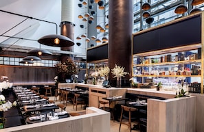 Interno di un ristorante moderno con soffitti alti, condotti a vista e un'area bar con una cantina.