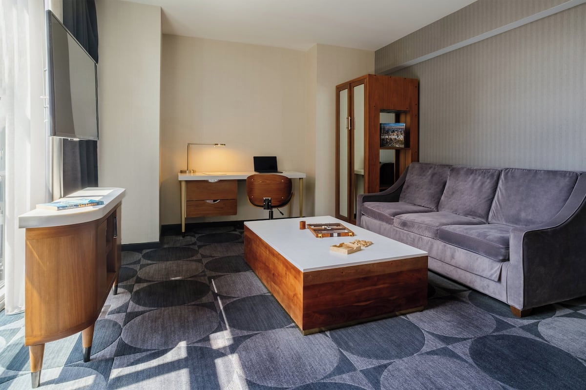 Ein modernes Hotelzimmer mit einem Holztisch, einem grauen Sofa, einem Couchtisch und einem gemusterten Teppich.