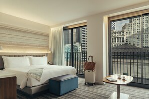 A hotel room with a large bed, a small table with a cup and a newspaper, a suitcase, and a view of a cityscape through a large window. - Park Terrace Hotel (New York)