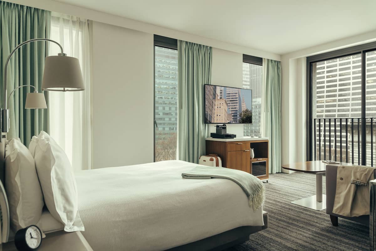 Habitación de hotel con una cama grande, un escritorio, un televisor y vistas a la ciudad desde la ventana.