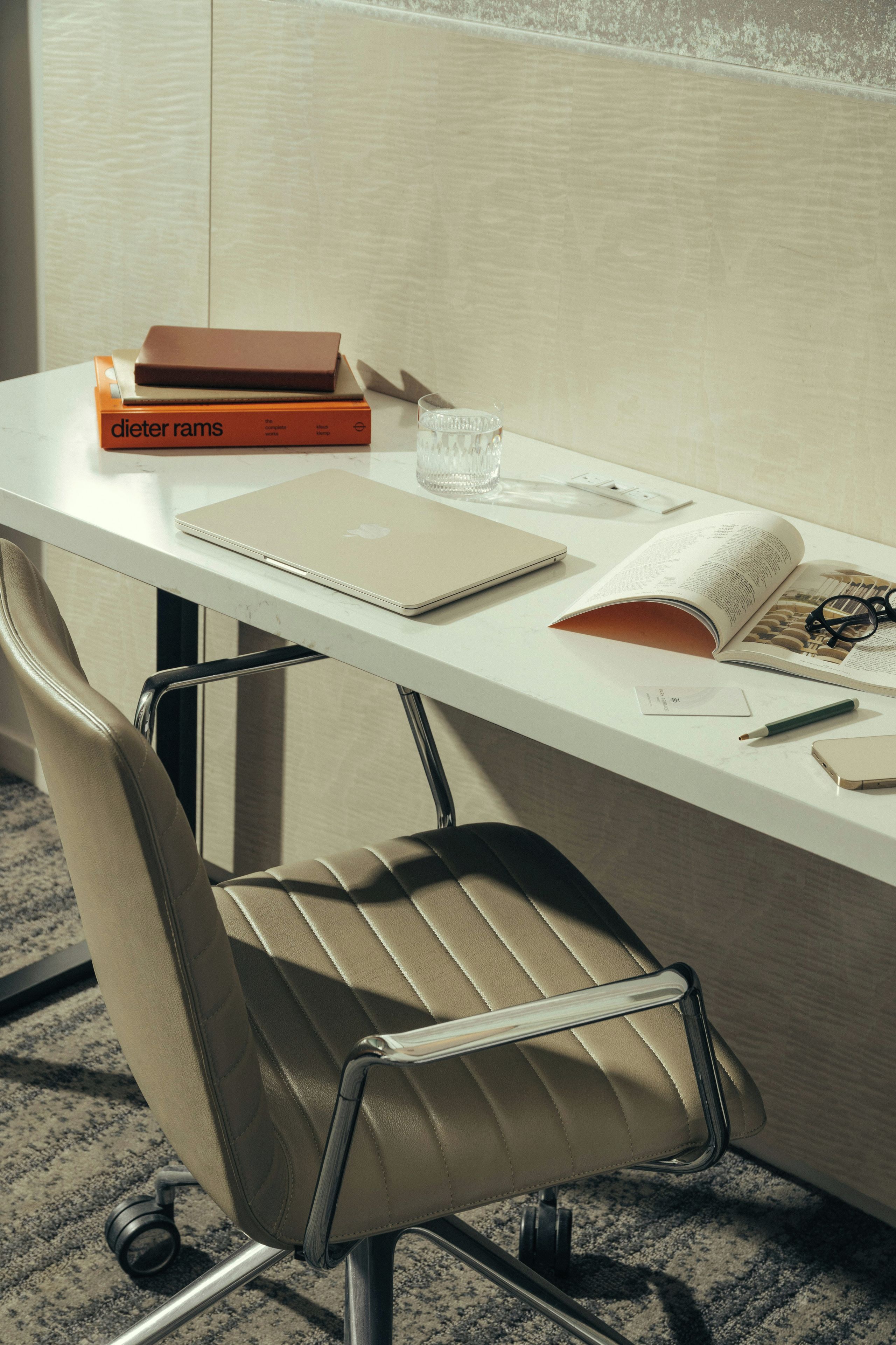Een modern bureau met een laptop, boeken, een bril en een pen.