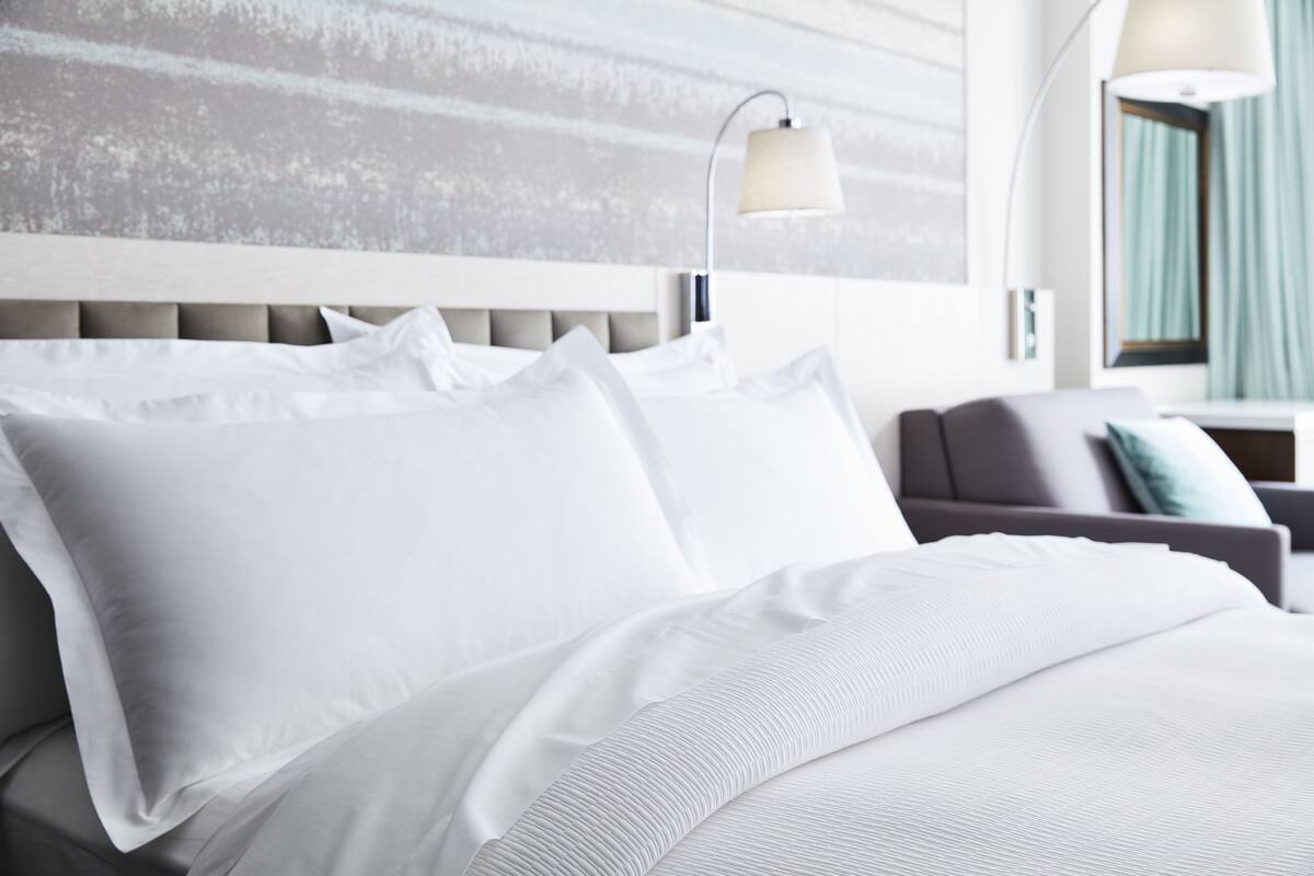 Una habitación de hotel moderna con una cama grande, un sofá gris y una lámpara fijada a la pared.