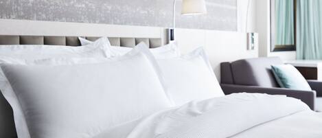 A modern hotel room with a large bed, a grey sofa, and a wall-mounted lamp.