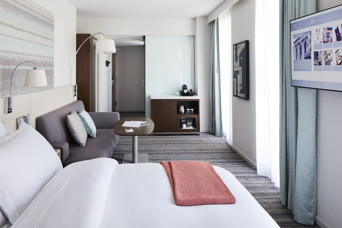 Habitación de hotel con cama, sofá, mesa de centro, escritorio y televisor.