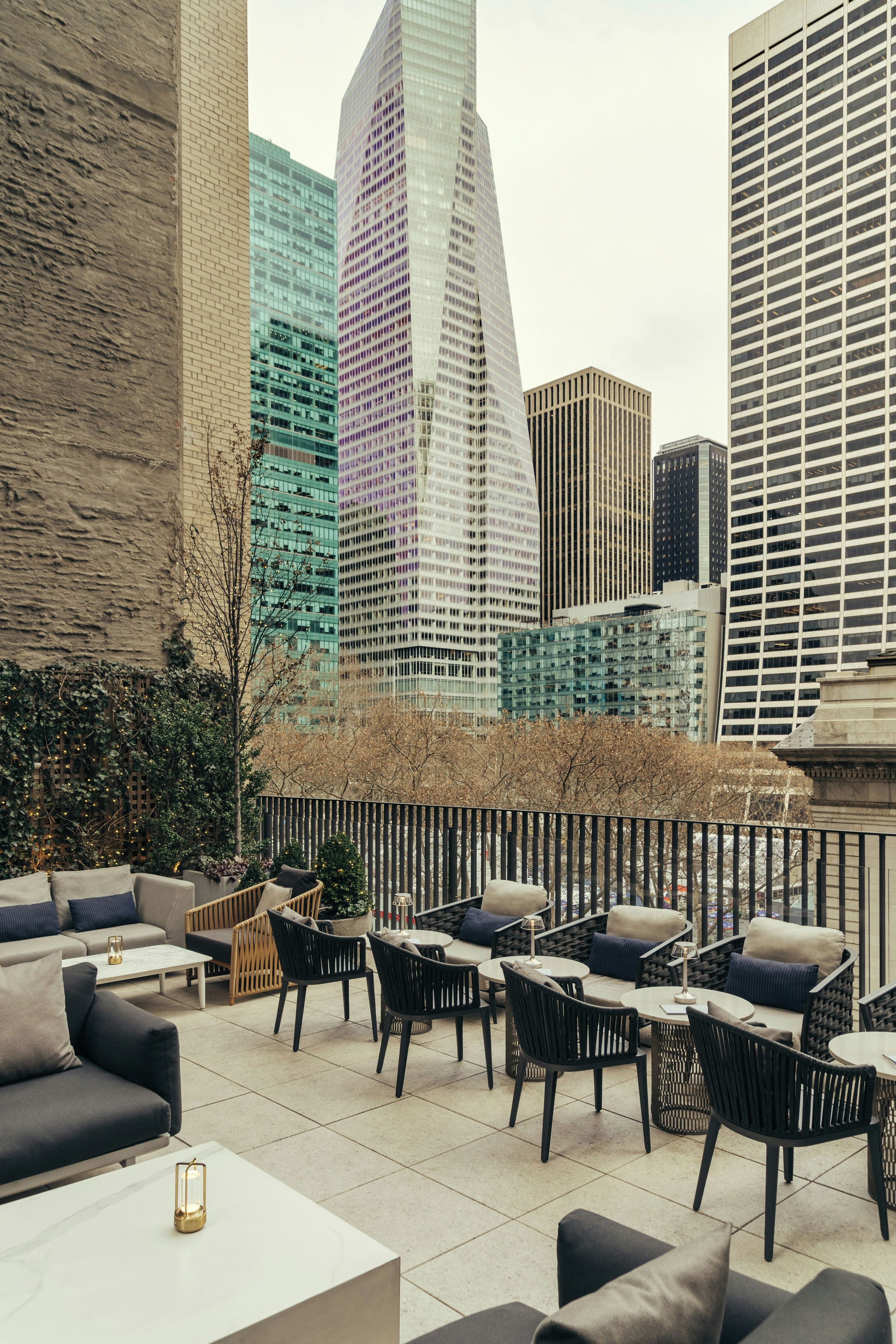 An outdoor seating area with modern furniture, a view of a city skyline, and a brick wall.