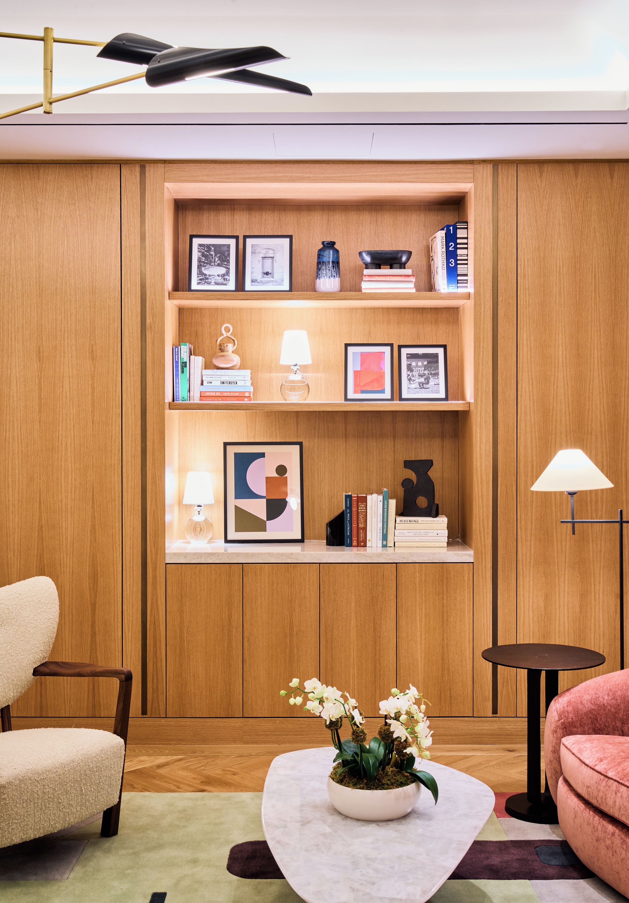 Una sala de estar moderna con una estantería de madera, una mesa redonda de centro con un arreglo floral y dos sillones.