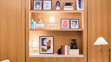 A modern living room with a wooden bookshelf, a round coffee table with a floral centerpiece, and two chairs.