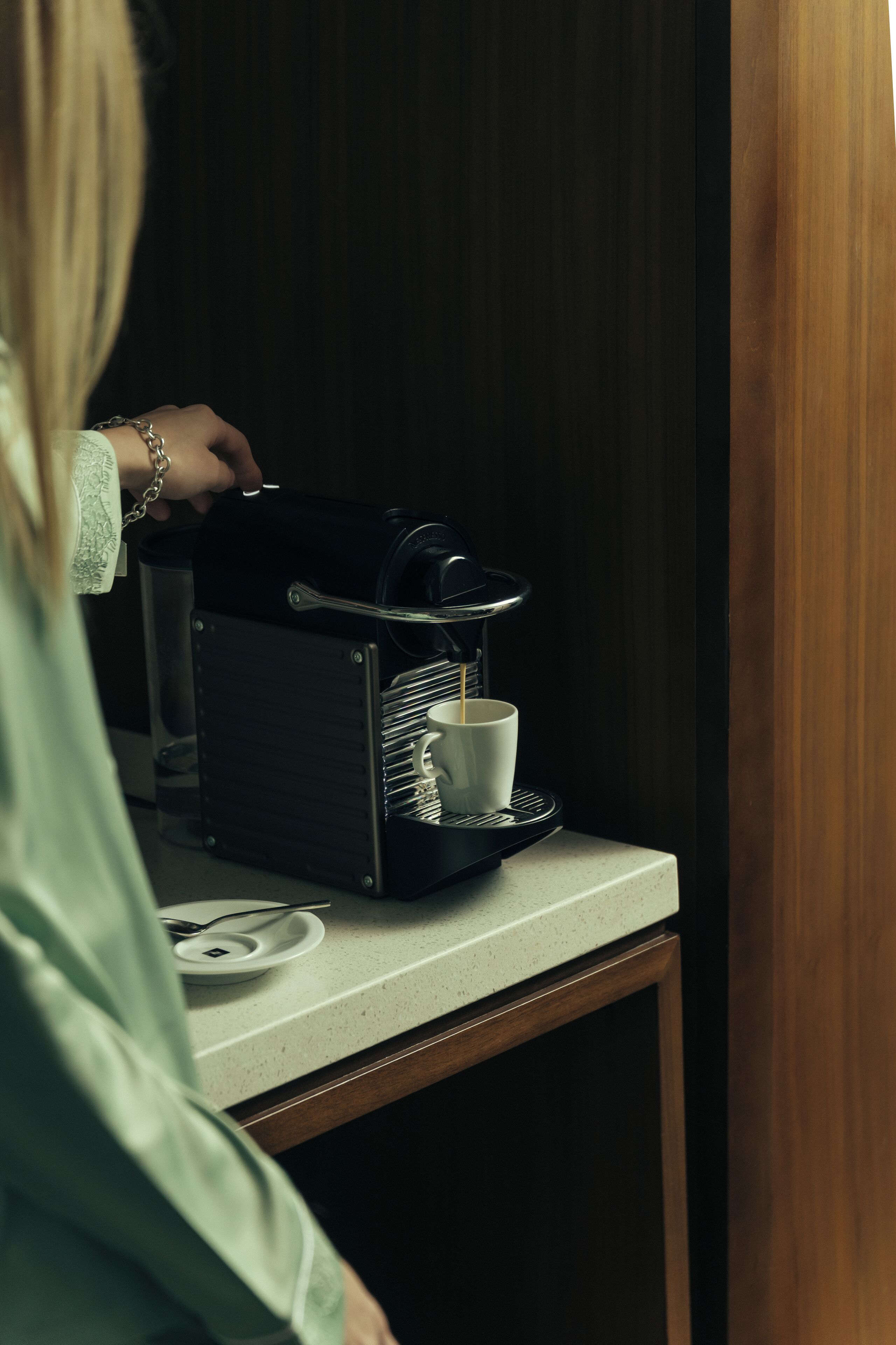 Una persona usando una máquina de café en una habitación con un armario de madera y una encimera blanca.
