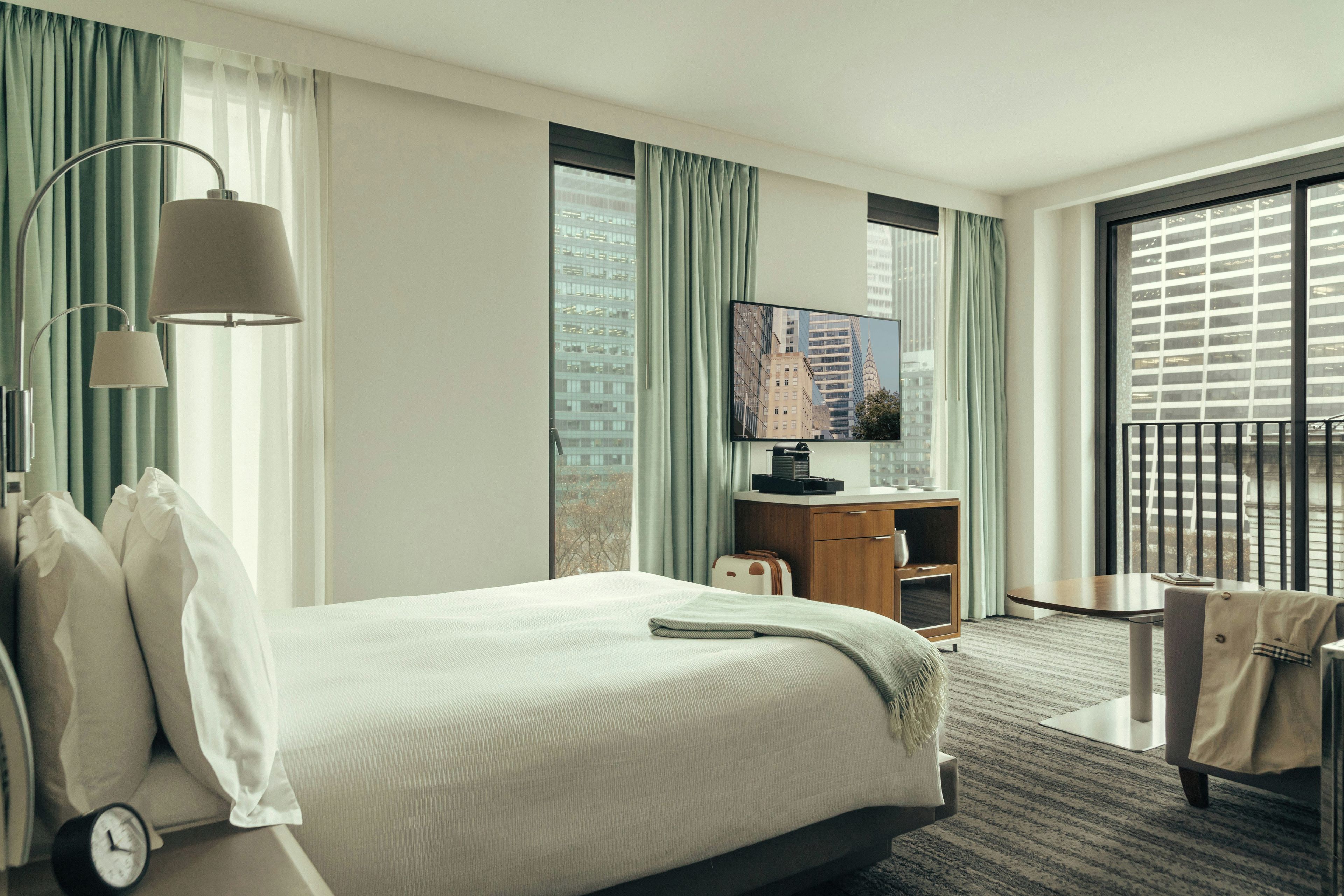 Ett hotellrum med en säng, ett skrivbord, en tv och utsikt över stadsbilden genom fönstret.